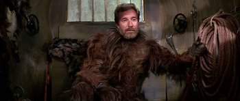 Movie still from “Barbarella” (1968), directed by Roger Vadim – A man with a beard is sitting on a couch; Medium shot, Over the shoulder angle