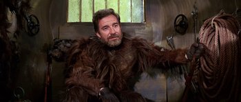 Movie still from “Barbarella” (1968), directed by Roger Vadim – A man with a beard is sitting in a room; Medium shot, Low angle