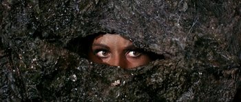 Movie still from “Barbarella” (1968), directed by Roger Vadim – A woman peeking out from behind a rock wall; Close Up shot, High angle