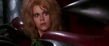 Movie still from “Barbarella” (1968), directed by Roger Vadim – A person sitting in a chair looking at the camera; Close Up shot, Over the shoulder angle