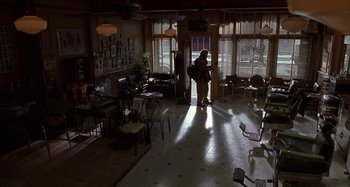 Movie still from “Barbershop” (2002), directed by Tim Story – A person standing in a room with chairs and tables; Wide shot, High angle