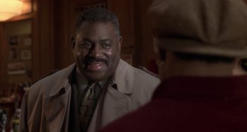 Movie still from “Barbershop” (2002), directed by Tim Story – A man in a trench coat smiles at the camera; Close Up shot, Over the shoulder angle