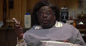 Movie still from “Barbershop” (2002), directed by Tim Story – A man with a beard and glasses talking to someone in a room; Close Up shot, Low angle