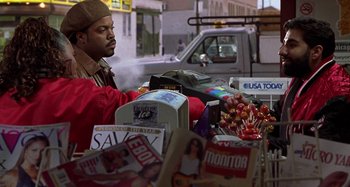 Movie still from “Barbershop” (2002), directed by Tim Story – A man standing in front of a pile of magazines; Medium shot, Over the shoulder angle