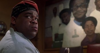 Movie still from “Barbershop” (2002), directed by Tim Story – A person in a room with a picture on the wall; Close Up shot, Low angle