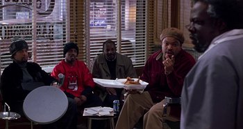Movie still from “Barbershop” (2002), directed by Tim Story – A group of men sitting around a table eating food; Medium shot, Over the shoulder angle