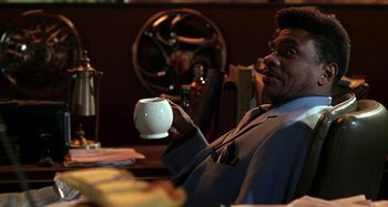 Movie still from “Barbershop” (2002), directed by Tim Story – A man sitting at a table holding a coffee cup; Medium shot, Low angle