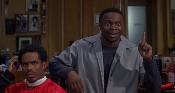 Movie still from “Barbershop” (2002), directed by Tim Story – A man standing next to another man in a barber shop; Medium shot, Over the shoulder angle