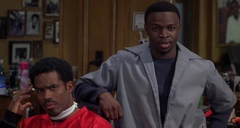 Movie still from “Barbershop” (2002), directed by Tim Story – A man standing next to another man in a room; Medium shot, Over the shoulder angle