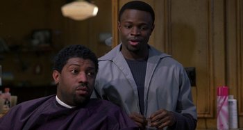 Movie still from “Barbershop” (2002), directed by Tim Story – A man getting his hair cut by another man; Medium shot, Over the shoulder angle