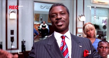 Movie still from “Barbershop 2: Back in Business” (2004), directed by Kevin Rodney Sullivan – A man wearing a suit and tie standing in front of a mirror; Close Up shot, Over the shoulder angle