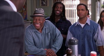 Movie still from “Barbershop 2: Back in Business” (2004), directed by Kevin Rodney Sullivan – A group of men standing next to each other in front of a table; Medium shot, Over the shoulder angle