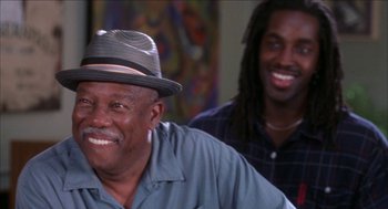 Movie still from “Barbershop 2: Back in Business” (2004), directed by Kevin Rodney Sullivan – Two men smiling for the camera in a room; Close Up shot, Over the shoulder angle
