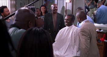 Movie still from “Barbershop 2: Back in Business” (2004), directed by Kevin Rodney Sullivan – A group of people standing around a man in a barber shop; Medium shot, Over the shoulder angle