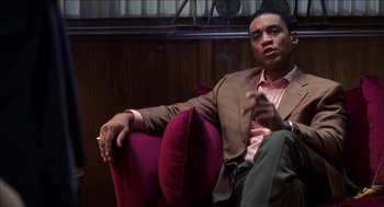 Movie still from “Barbershop 2: Back in Business” (2004), directed by Kevin Rodney Sullivan – A man sitting on a chair smoking a cigarette; Medium shot, Low angle