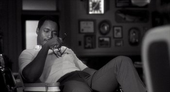 Movie still from “Barbershop 2: Back in Business” (2004), directed by Kevin Rodney Sullivan – A black and white photo of a man holding a pair of glasses; Medium shot, Low angle