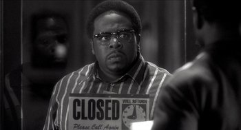Movie still from “Barbershop 2: Back in Business” (2004), directed by Kevin Rodney Sullivan – A black and white photo of a man holding a closed sign; Close Up shot, Low angle
