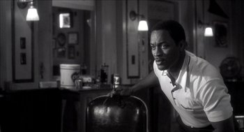 Movie still from “Barbershop 2: Back in Business” (2004), directed by Kevin Rodney Sullivan – A black and white photo of a man leaning on a barrel; Medium shot, Over the shoulder angle