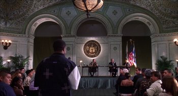 Movie still from “Barbershop 2: Back in Business” (2004), directed by Kevin Rodney Sullivan – A man standing in front of two people in front of a microphone; Wide shot, Over the shoulder angle