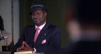 Movie still from “Barbershop 2: Back in Business” (2004), directed by Kevin Rodney Sullivan – A man in a suit and hat is smiling for the camera; Close Up shot, Over the shoulder angle