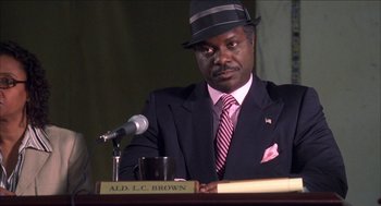 Movie still from “Barbershop 2: Back in Business” (2004), directed by Kevin Rodney Sullivan – A man wearing a suit and tie sitting in front of a microphone; Close Up shot, Low angle