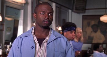 Movie still from “Barbershop 2: Back in Business” (2004), directed by Kevin Rodney Sullivan – A man in a blue jacket standing in front of other people; Close Up shot, Over the shoulder angle