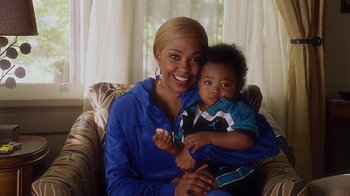 Movie still from “Barbershop: The Next Cut” (2016), directed by Malcolm D. Lee – A woman holding a baby in her arms and smiling; Medium shot, High angle