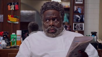 Movie still from “Barbershop: The Next Cut” (2016), directed by Malcolm D. Lee – A man with a beard and glasses is reading a newspaper; Close Up shot, Low angle
