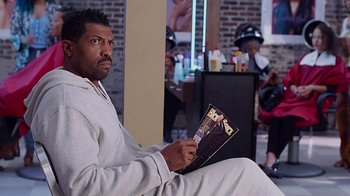 Movie still from “Barbershop: The Next Cut” (2016), directed by Malcolm D. Lee – A man sitting in front of a mirror holding a magazine; Medium shot, Over the shoulder angle