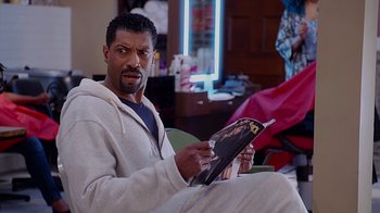 Movie still from “Barbershop: The Next Cut” (2016), directed by Malcolm D. Lee – A man sitting on a chair holding a magazine; Close Up shot, Over the shoulder angle
