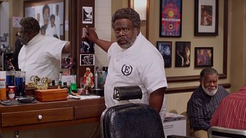 Movie still from “Barbershop: The Next Cut” (2016), directed by Malcolm D. Lee – A man in a barber shop with a black chair in front of him; Medium shot, Over the shoulder angle