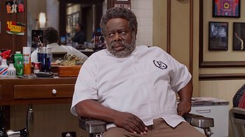 Movie still from “Barbershop: The Next Cut” (2016), directed by Malcolm D. Lee – A man sitting in a barber chair with a beard; Medium shot, Over the shoulder angle