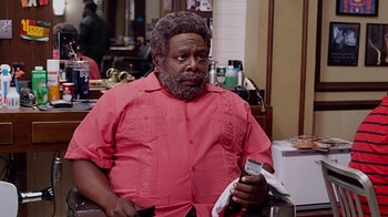 Movie still from “Barbershop: The Next Cut” (2016), directed by Malcolm D. Lee – A man with a beard and a pink shirt is looking at his cell phone; Medium shot, Over the shoulder angle
