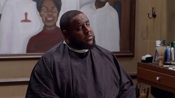 Movie still from “Barbershop: The Next Cut” (2016), directed by Malcolm D. Lee – A man sitting in front of a painting of a woman; Close Up shot, Over the shoulder angle