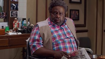 Movie still from “Barbershop: The Next Cut” (2016), directed by Malcolm D. Lee – A man sitting at a table holding a newspaper; Medium shot, Over the shoulder angle