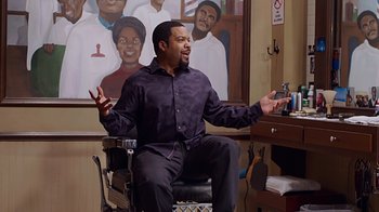 Movie still from “Barbershop: The Next Cut” (2016), directed by Malcolm D. Lee – A man sitting in front of a painting of a woman; Medium shot, Over the shoulder angle