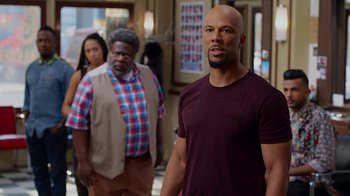 Movie still from “Barbershop: The Next Cut” (2016), directed by Malcolm D. Lee – A man standing in front of a group of people; Medium shot, Over the shoulder angle