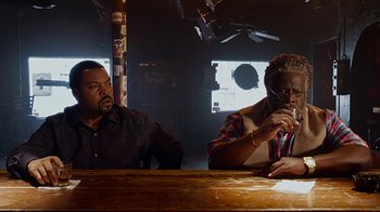 Movie still from “Barbershop: The Next Cut” (2016), directed by Malcolm D. Lee – Two people sitting at a table in a room; Medium shot, Over the shoulder angle