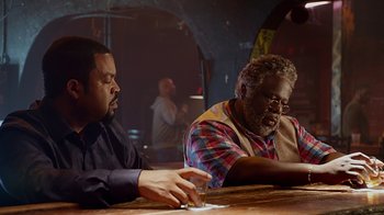 Movie still from “Barbershop: The Next Cut” (2016), directed by Malcolm D. Lee – Two men sitting at a table in front of each other; Medium shot, Over the shoulder angle