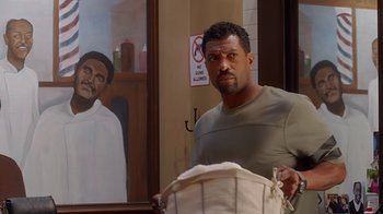 Movie still from “Barbershop: The Next Cut” (2016), directed by Malcolm D. Lee – A man standing next to a painting of a person; Medium shot, Over the shoulder angle