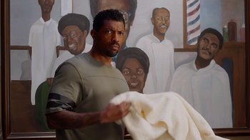 Movie still from “Barbershop: The Next Cut” (2016), directed by Malcolm D. Lee – A man holding a towel in front of a painting; Medium shot, Over the shoulder angle