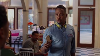 Movie still from “Barbershop: The Next Cut” (2016), directed by Malcolm D. Lee – A man holding a cell phone while standing next to another man; Medium shot, Over the shoulder angle