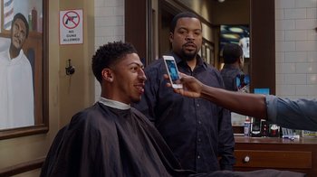 Movie still from “Barbershop: The Next Cut” (2016), directed by Malcolm D. Lee – A man in a barber shop taking a picture of another man in a barber chair; Medium shot, Over the shoulder angle