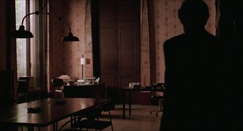 Movie still from “Barcelona” (1994), directed by Whit Stillman – A man standing in a room with a desk and a chair; Wide shot, Over the shoulder angle