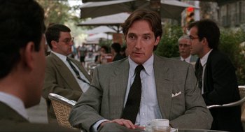 Movie still from “Barcelona” (1994), directed by Whit Stillman – A man in a suit and tie sitting at an outdoor table; Close Up shot, Over the shoulder angle