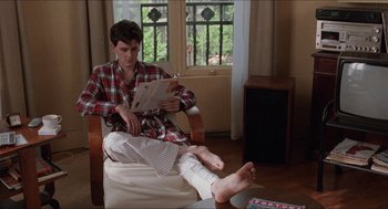 Movie still from “Barcelona” (1994), directed by Whit Stillman – A young man sitting in a chair reading a magazine; Medium shot, High angle