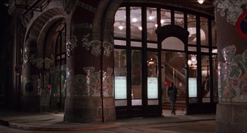 Movie still from “Barcelona” (1994), directed by Whit Stillman – A person walking in front of a building with many windows; Extreme Wide shot, Low angle
