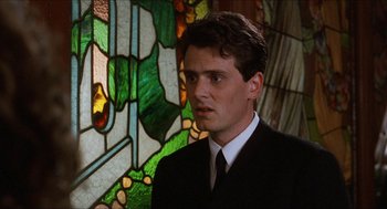 Movie still from “Barcelona” (1994), directed by Whit Stillman – A man in a suit and tie standing in front of a stained glass window; Close Up shot, Low angle