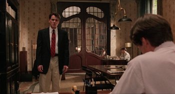 Movie still from “Barcelona” (1994), directed by Whit Stillman – A man in a suit and tie standing in front of a table; Medium shot, Over the shoulder angle