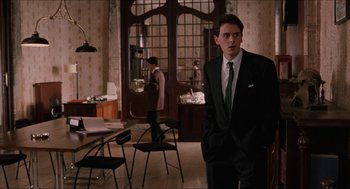 Movie still from “Barcelona” (1994), directed by Whit Stillman – A man in a suit standing in front of a table; Medium shot, Over the shoulder angle